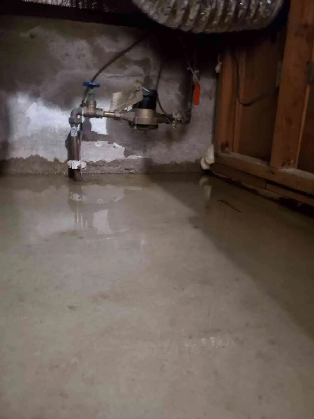 A flooded basement with a partially submerged air conditioning unit or similar piece of equipment, and water covering the floor.