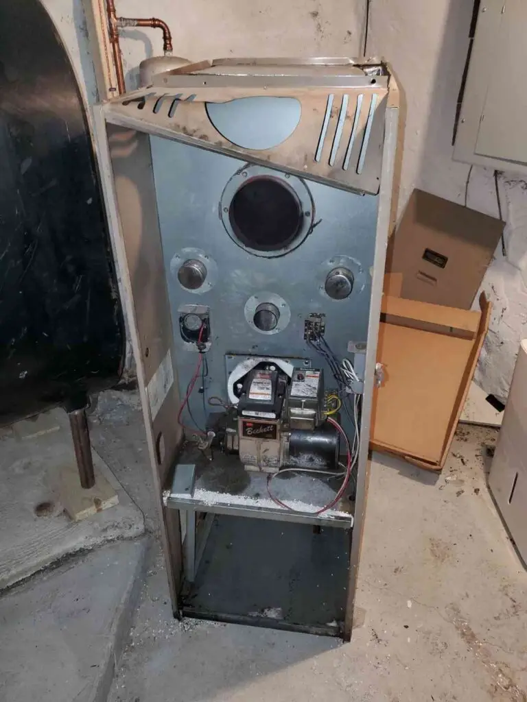 An image showing the interior of a building with a damaged furnace or appliance. The furnace has various components and wiring exposed, indicating it is in need of repair or replacement.