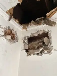 An image showing extensive damage and holes in a wall, with exposed wooden framing and crumbling drywall or plaster.