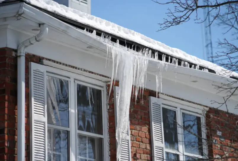 A snowy roof with icicles hanging from the edge of a brick house