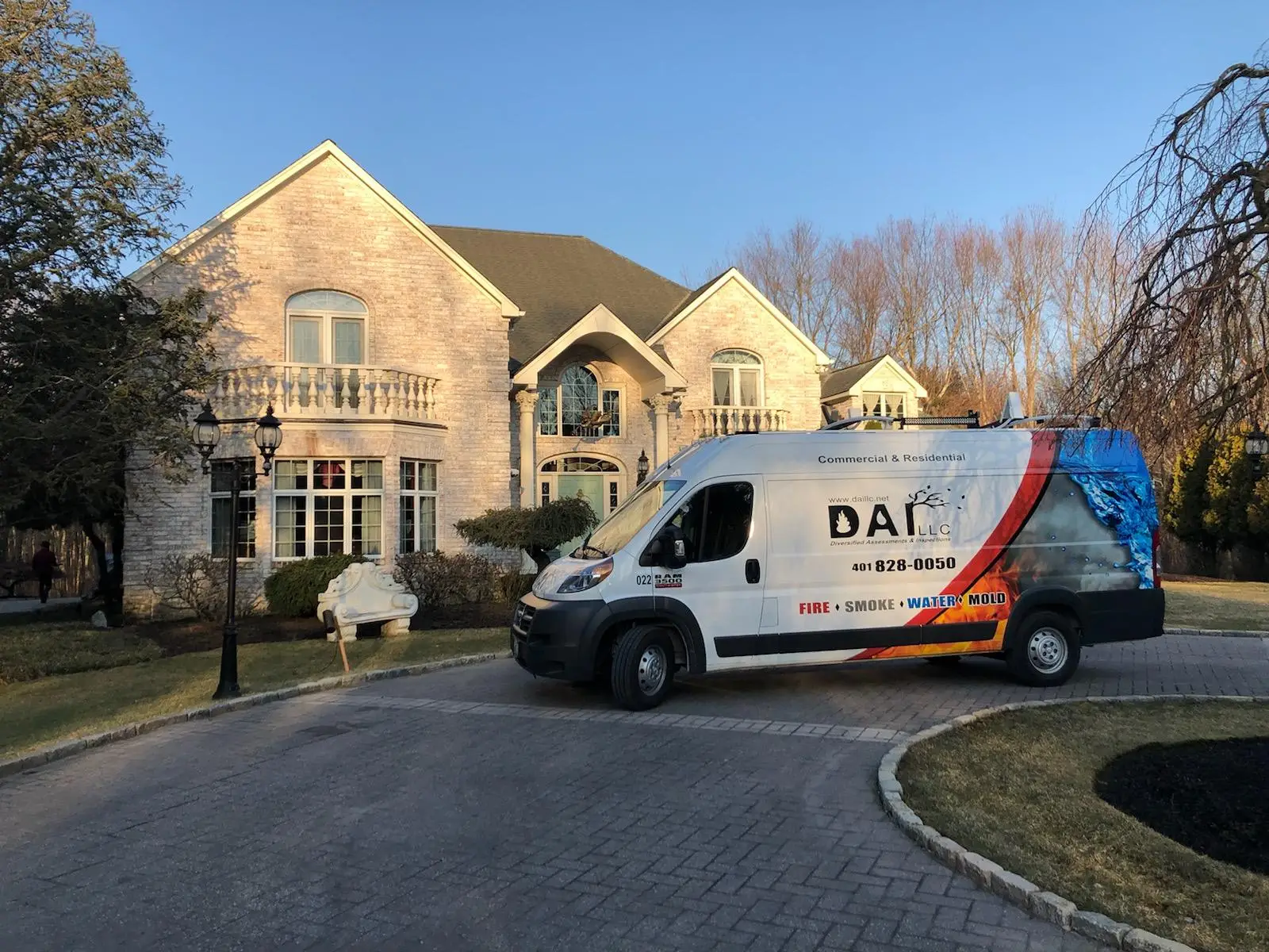 A large brick residential building with balconies and arched windows, alongside a white commercial van with the company name 'DAI LLC' and services listed on the side.