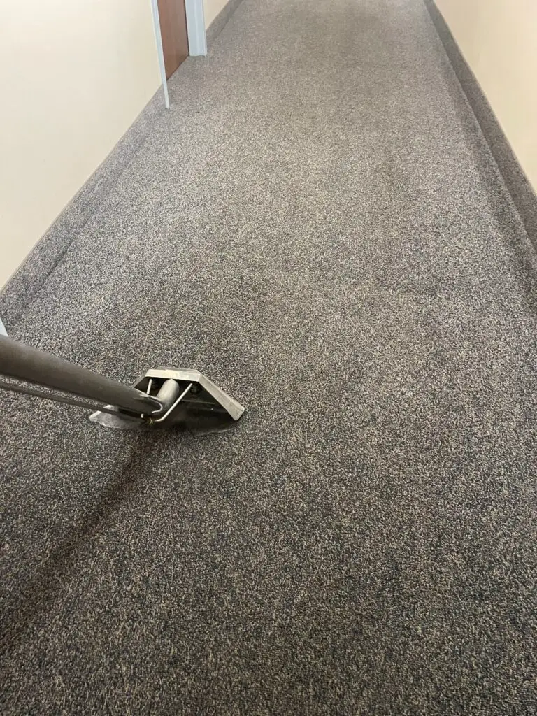 A long, narrow hallway with a gray, speckled floor and a tile wall visible in the distance.