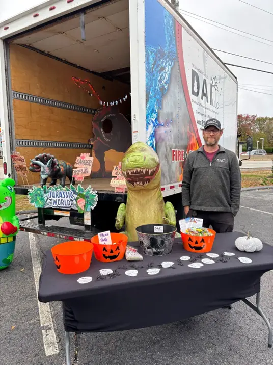 DAI employee at a Dinosaur themed DAI Truck to hand out candy at a local trunk-or-treat event